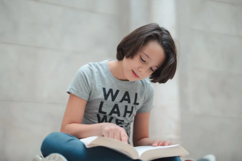 a twelve year old boy reading a book wearing Wallah We Can T-shirt